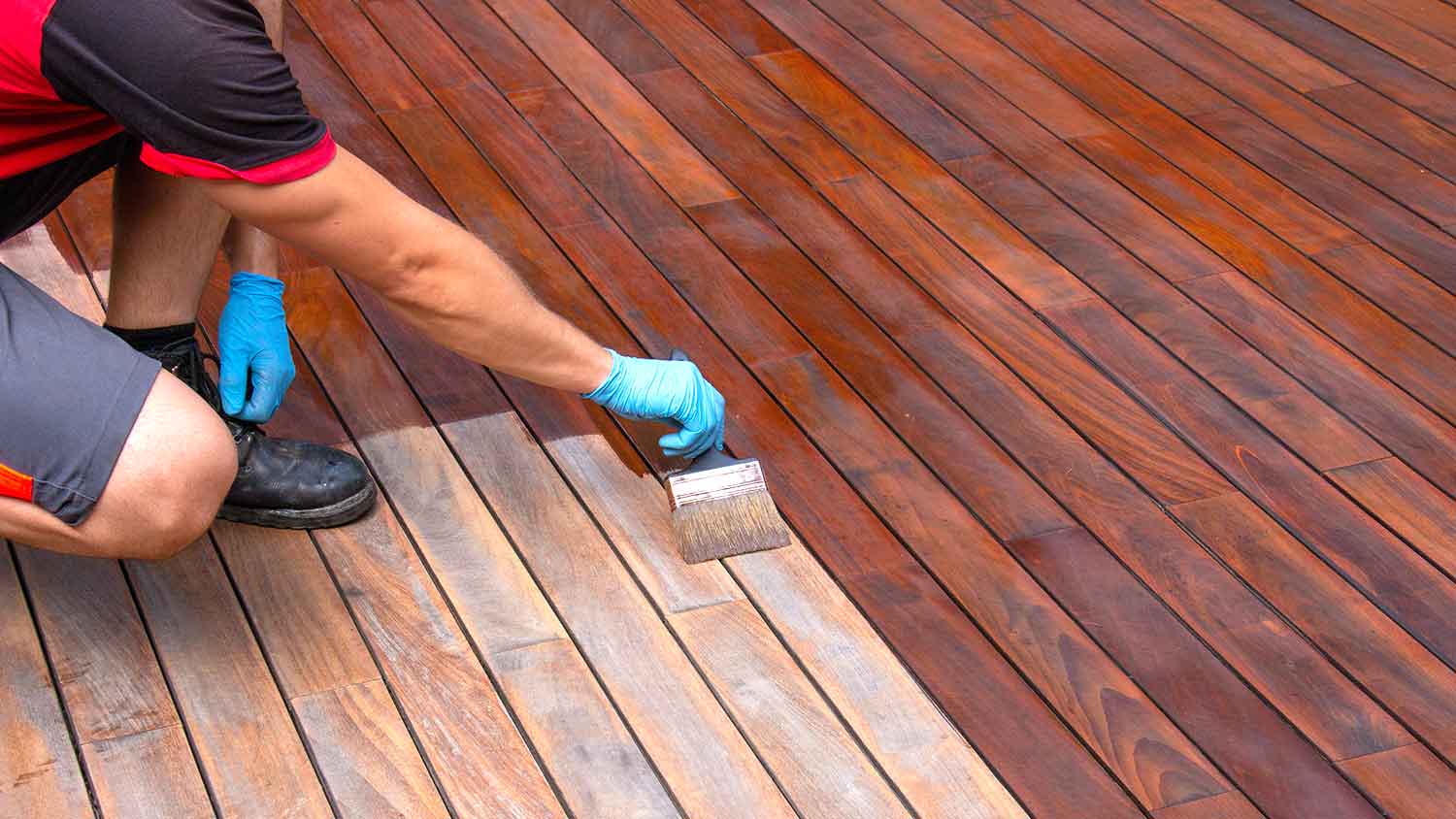 Worker using brush to stain a wooden patio deck