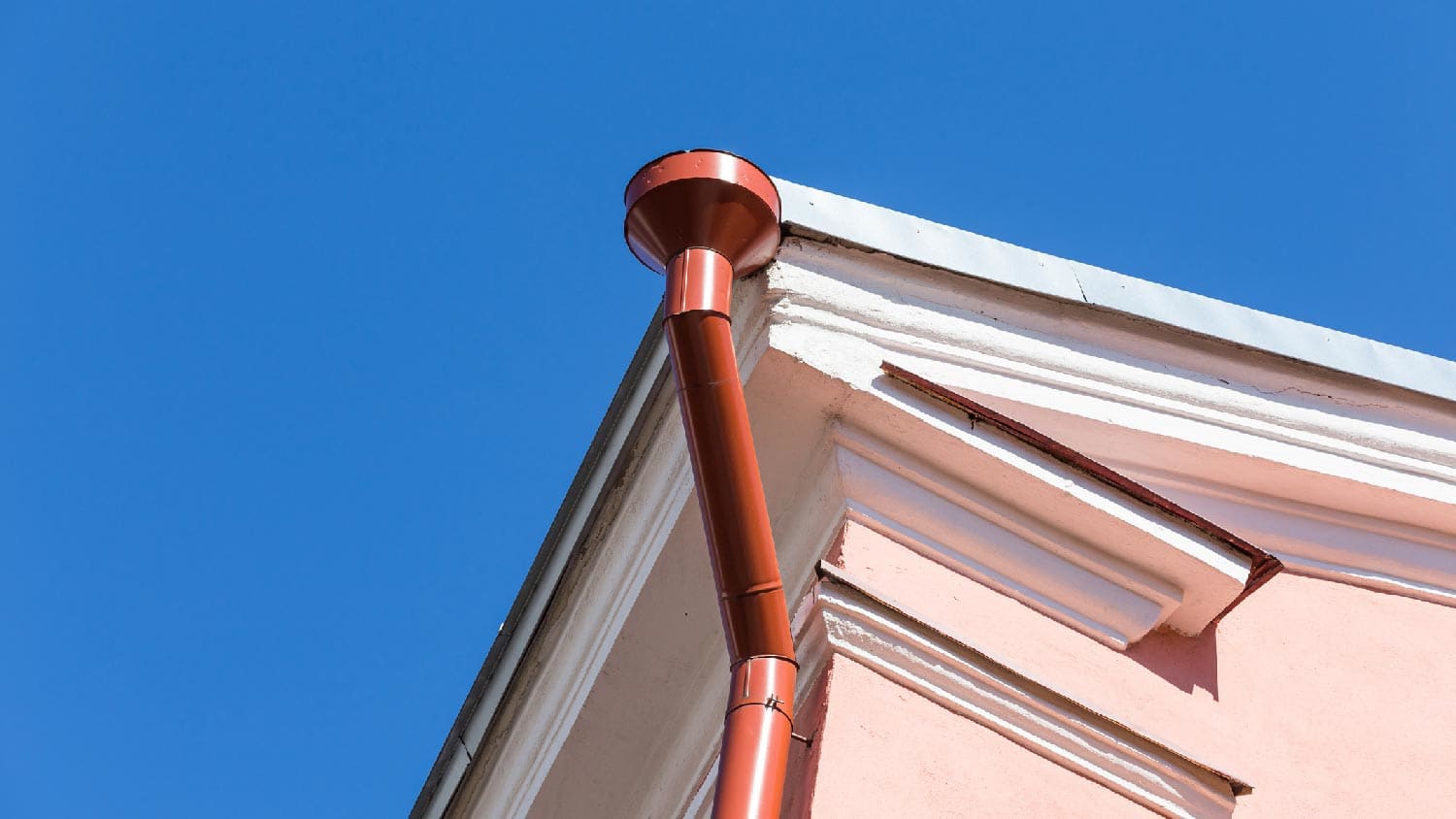 A gutter and downspout of a house against the blue sky