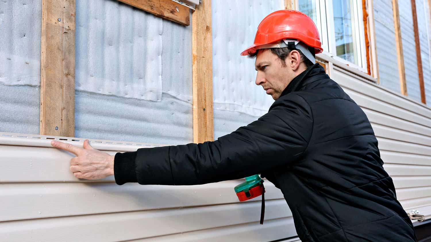 worker installing beige siding on house