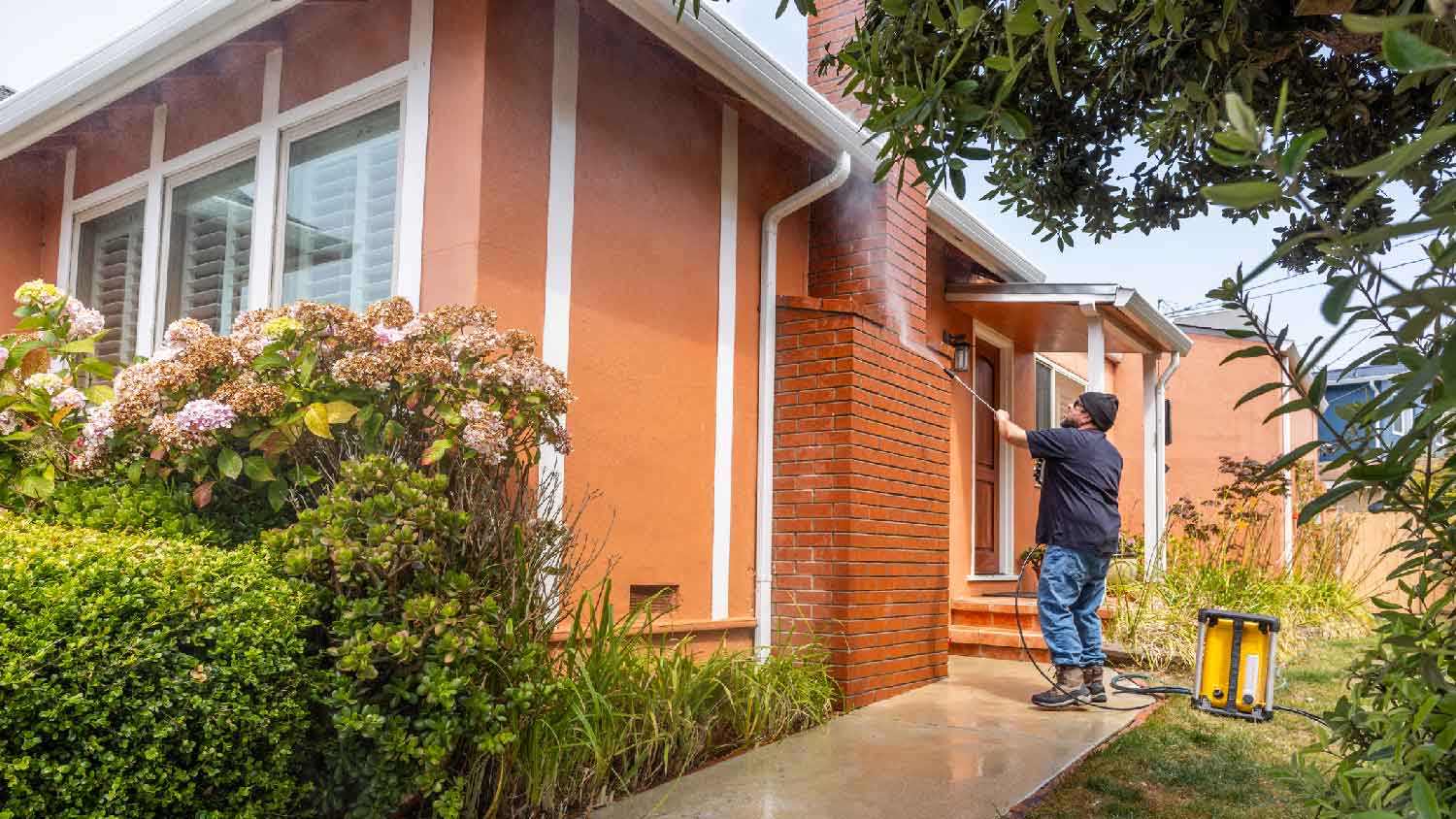 A man pressure washing the exterior of a house