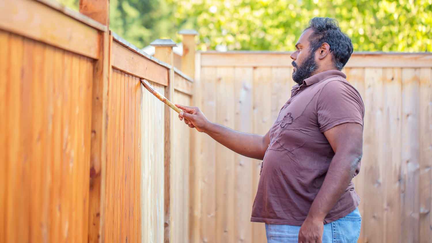 Man using brush to stain a wooden fence