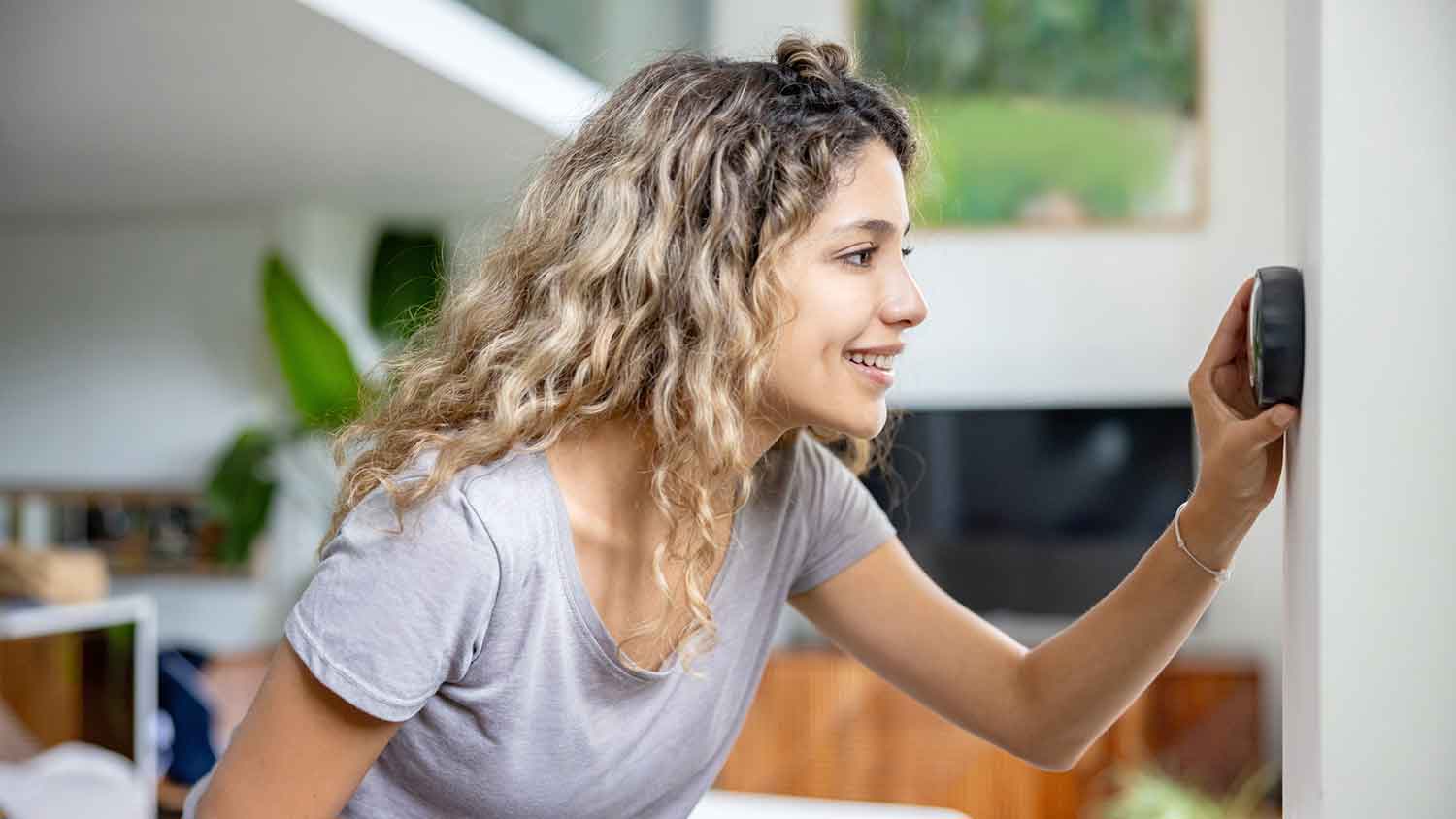 Woman adjusting thermostat installed in the living room
