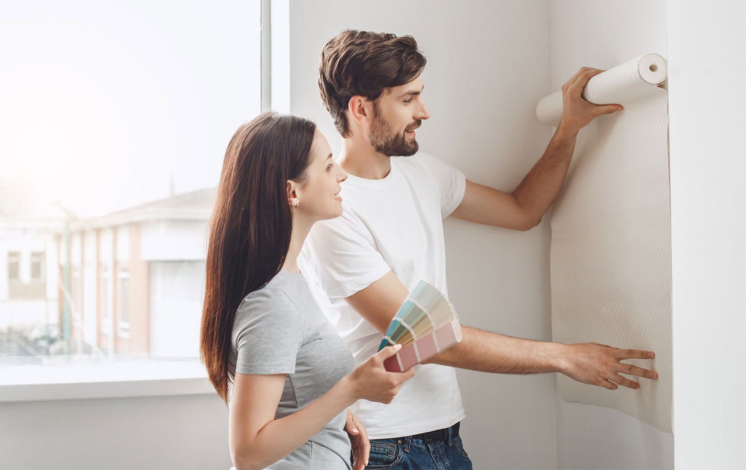 Young couple holding wallpaper roll against the wall