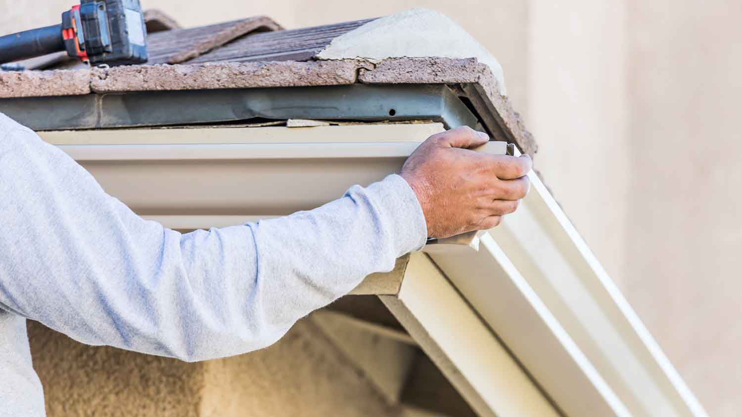 Worker installing aluminum gutters on the house