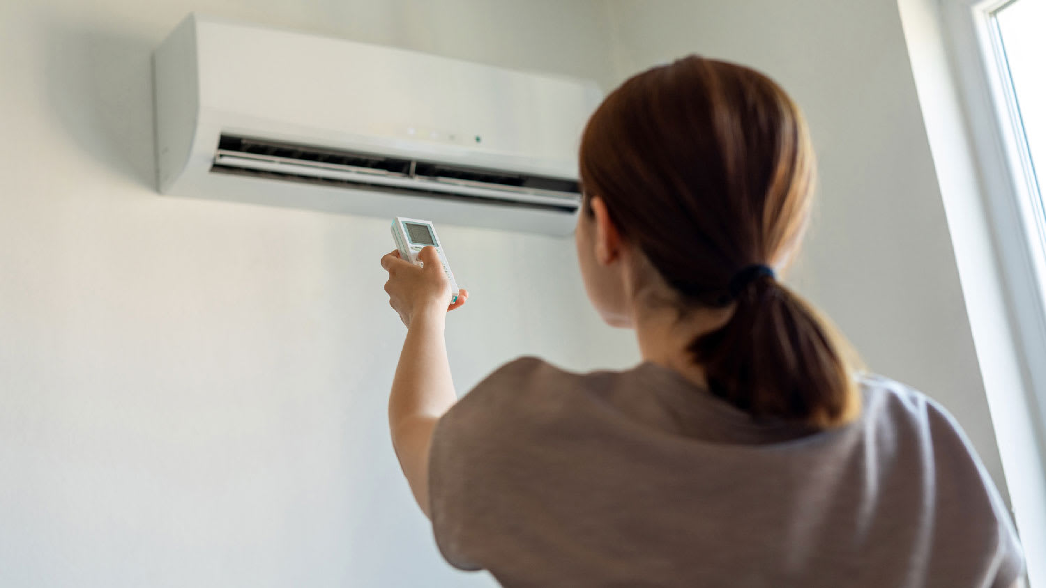 Woman turning on split-AC unit with remote