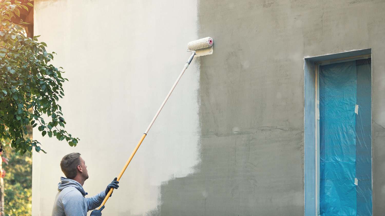 A professional painting a house wall with a roller