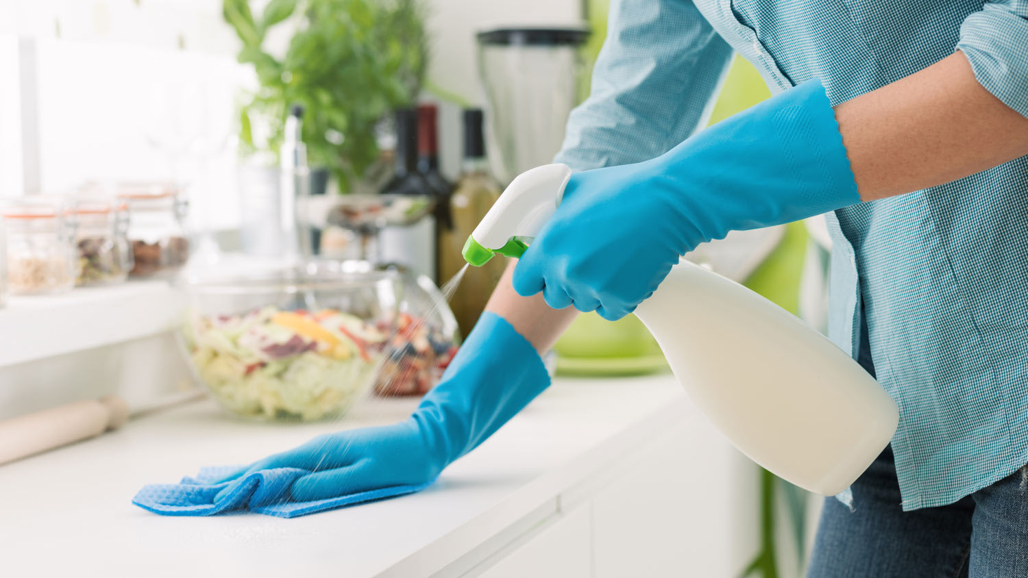 A woman in protective gloves cleaning using a spray detergent