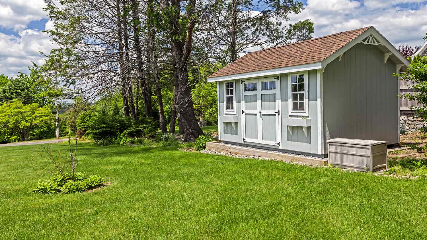 Grey garden shed in backyard with brown shingle roof