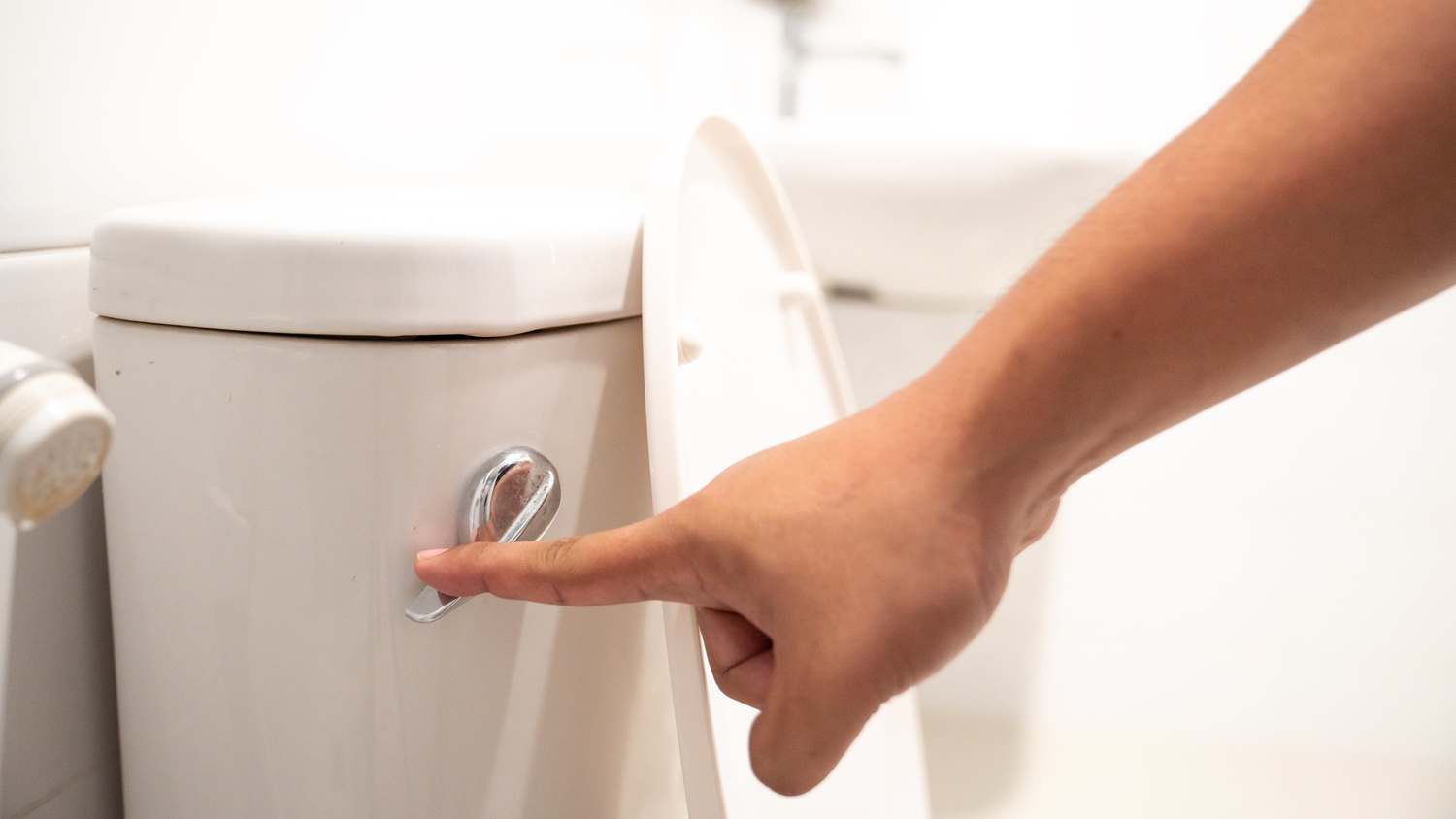 A close-up of a hand flushing a toilet