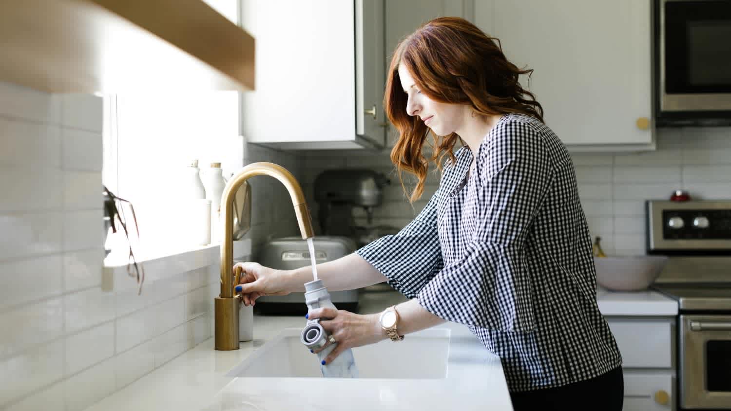 Woman filling water bottle in kitchen sink