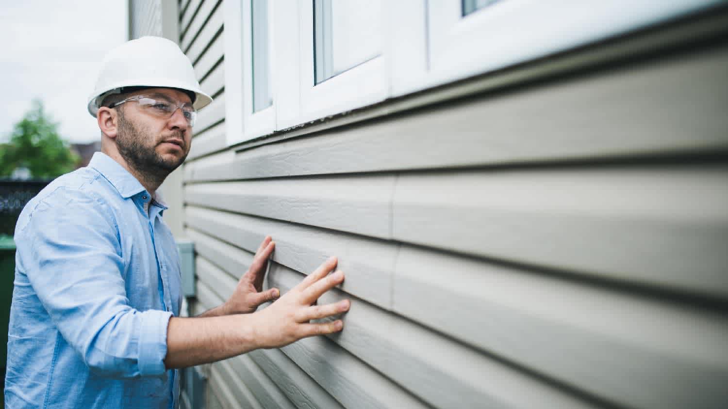 A person inspecting the vinyl siding of a house