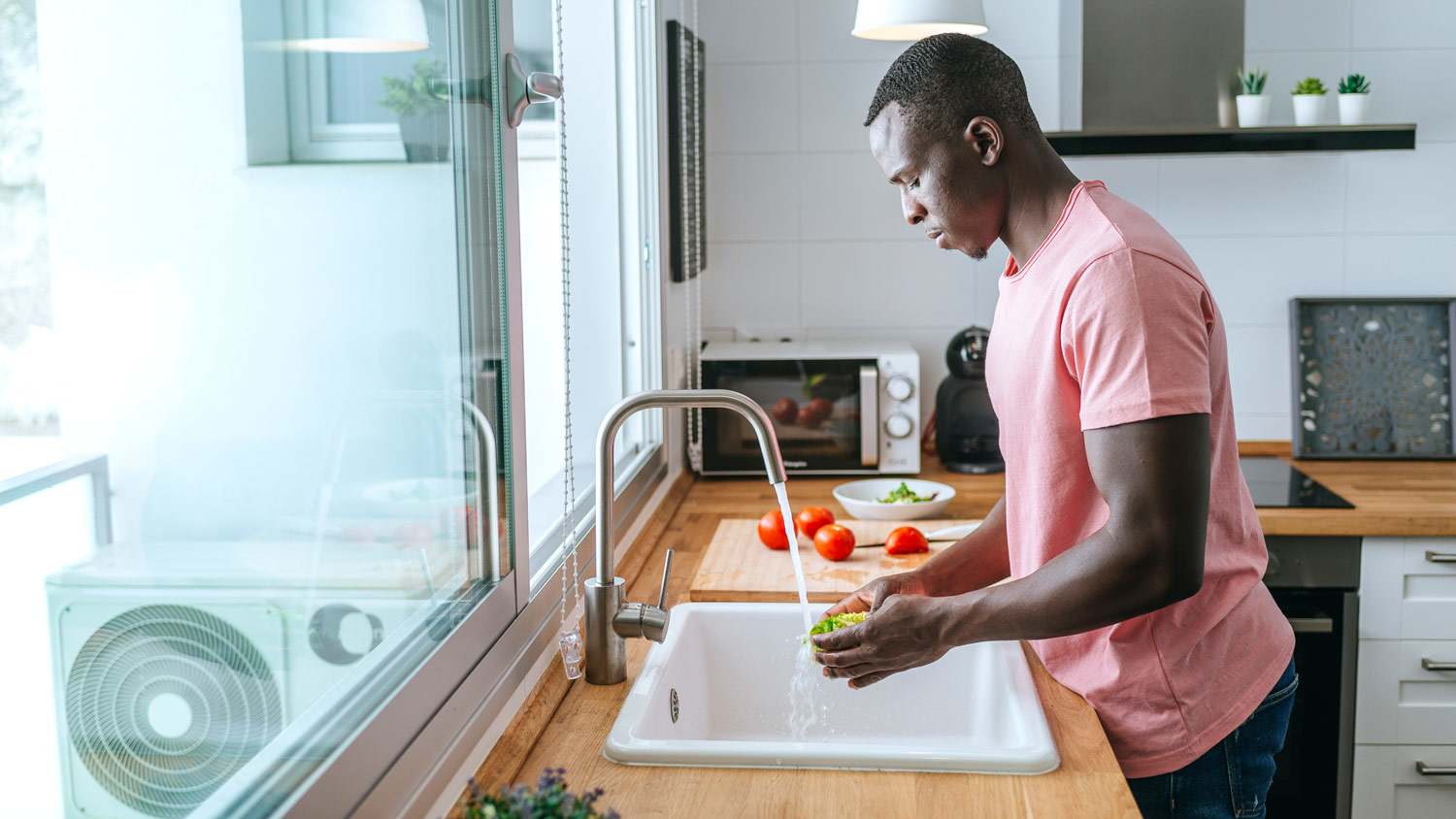 A young man washing vegetables in a kitchen sink