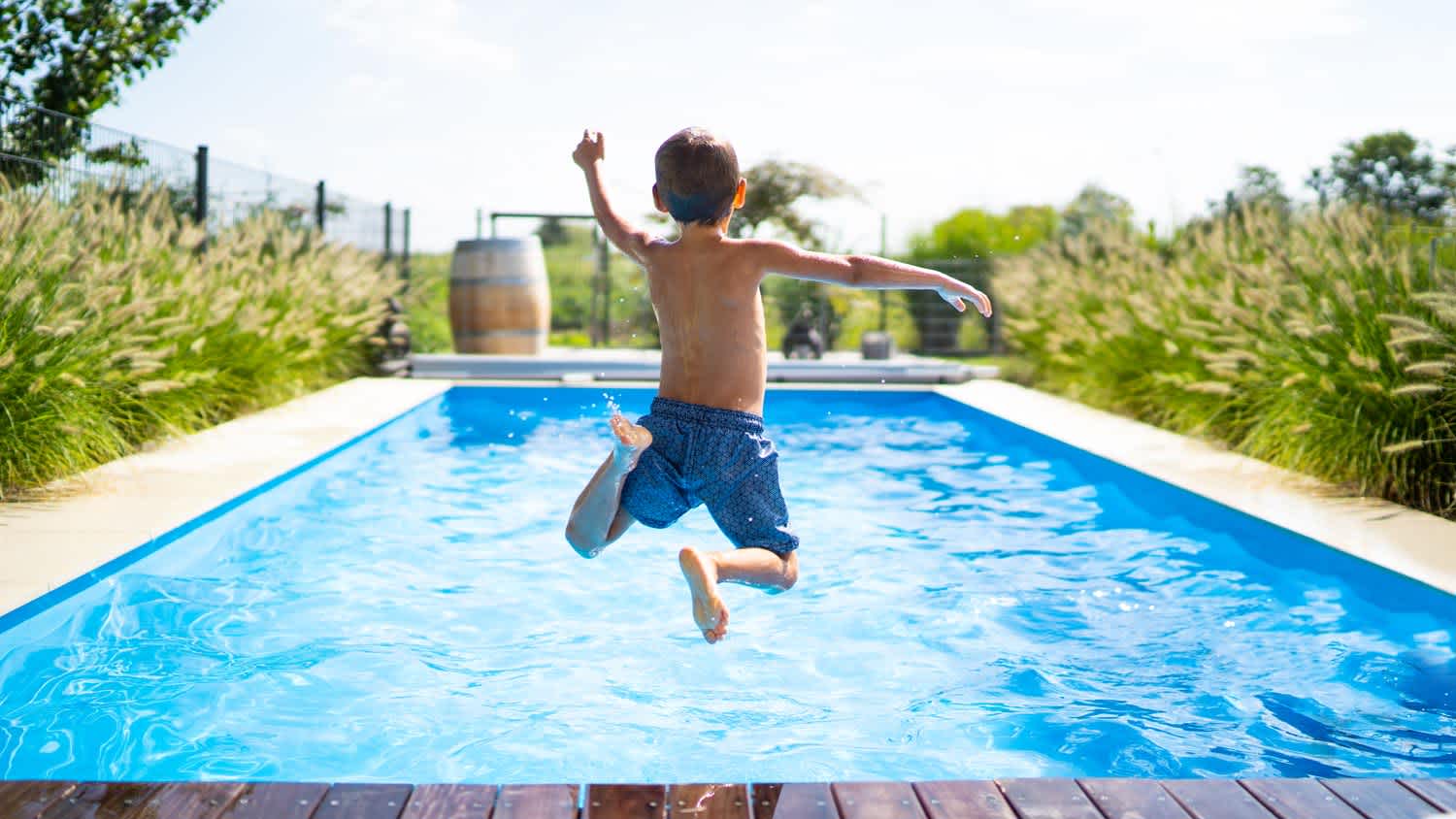 A boy jumping in a pool happily on a sunny day