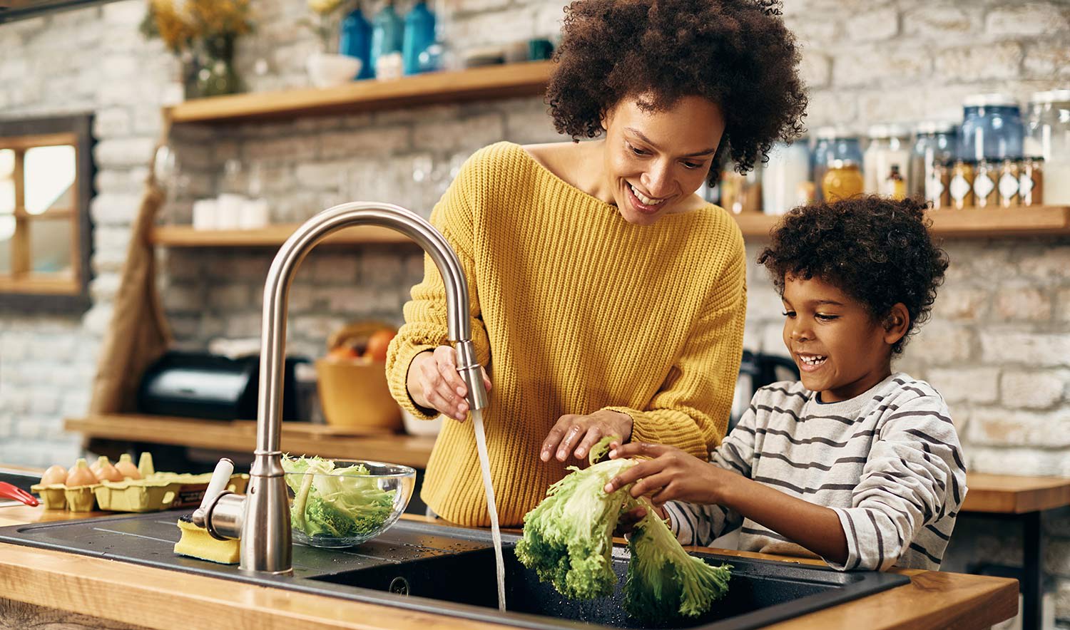 Mother helps her son wash off lettuce in the sink