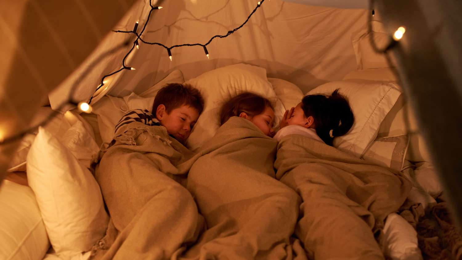 Three children sleeping together covered in a blanket