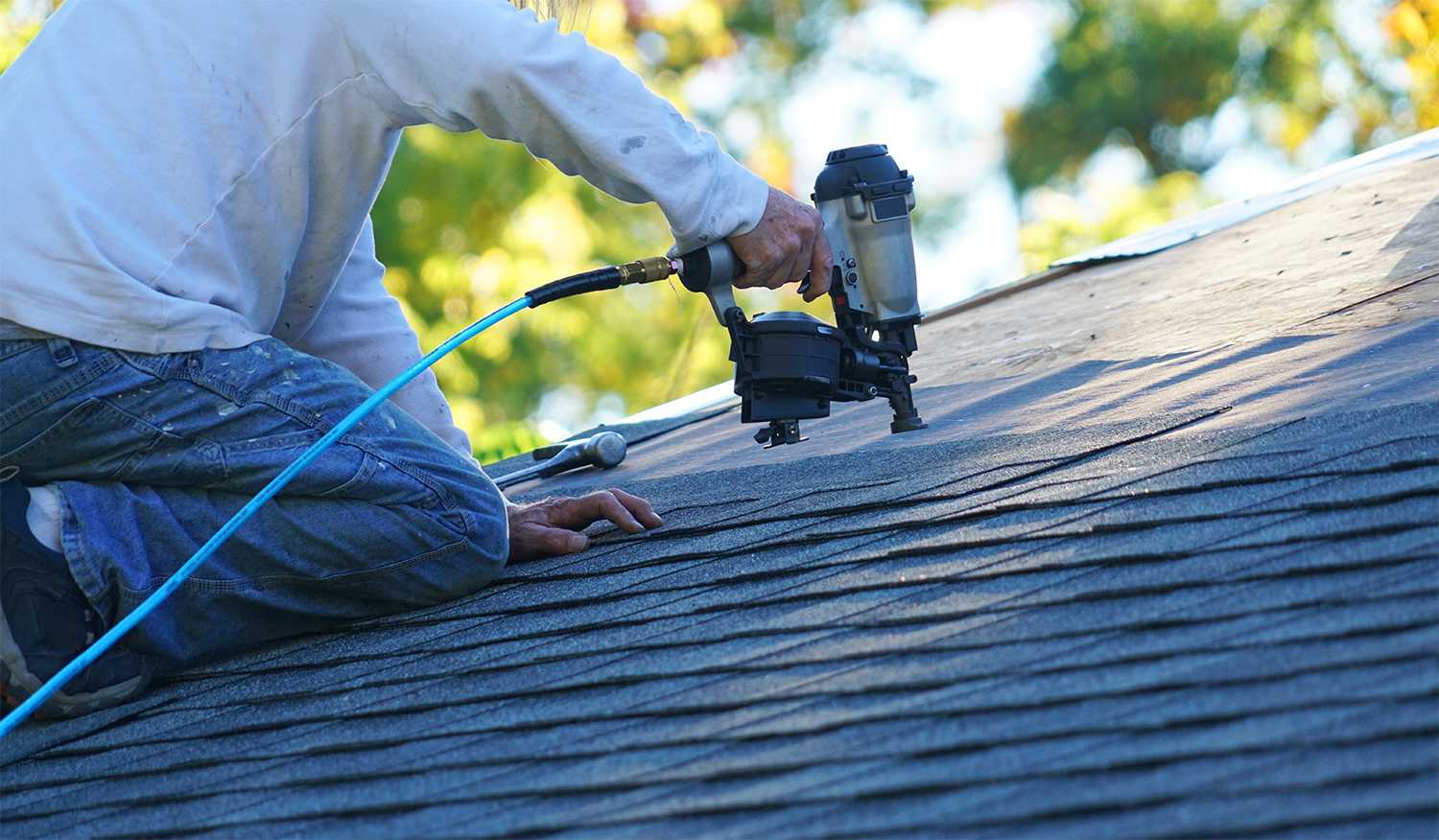 Person putting shingles on with nail gun