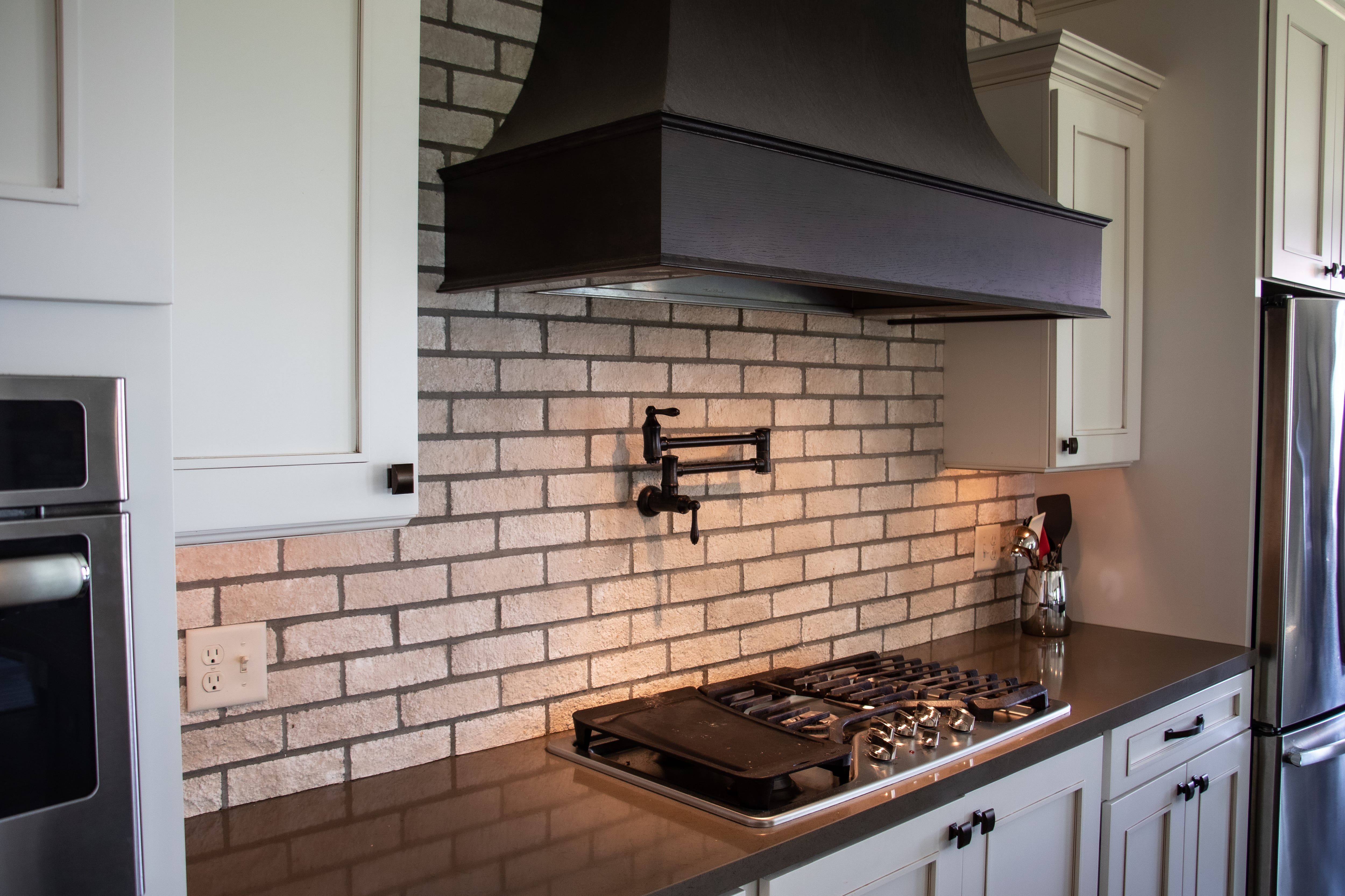A traditional kitchen with a pot filler faucet and a large hood vent over a gas stove