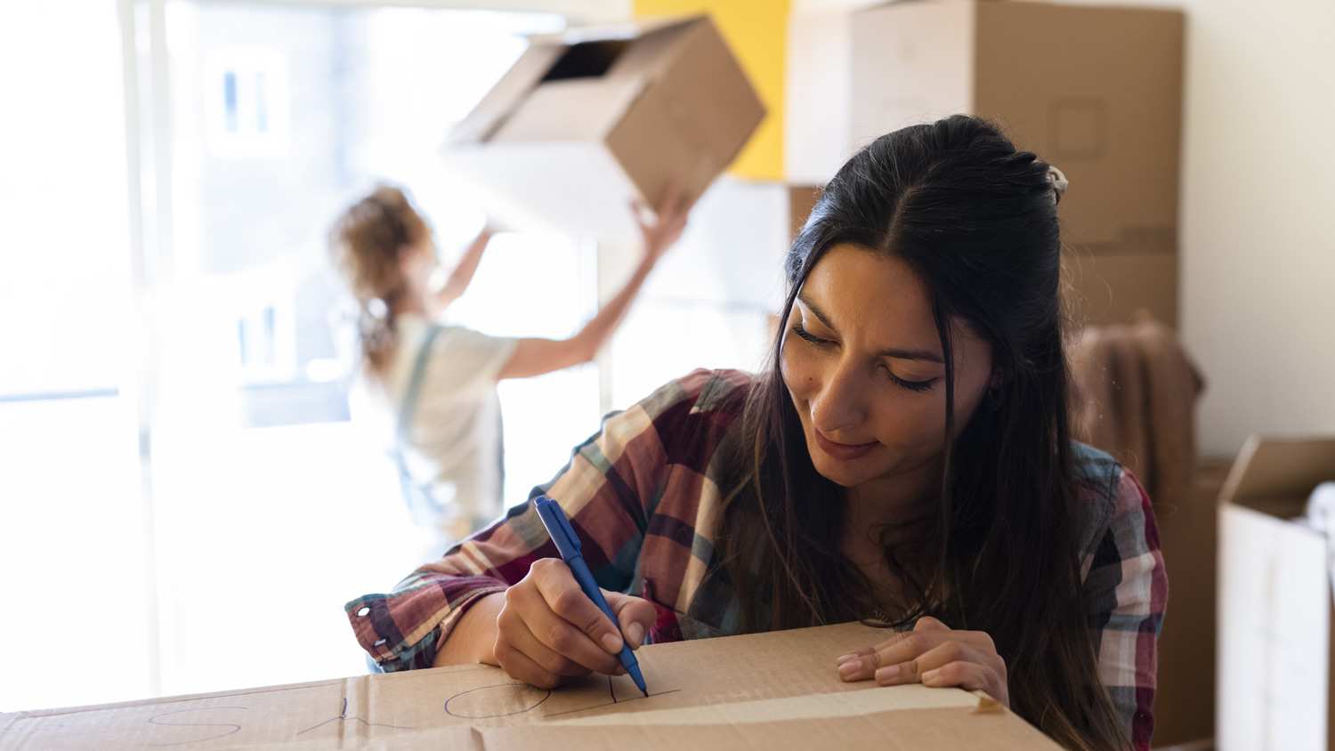 A woman writing labels on cardboard boxes