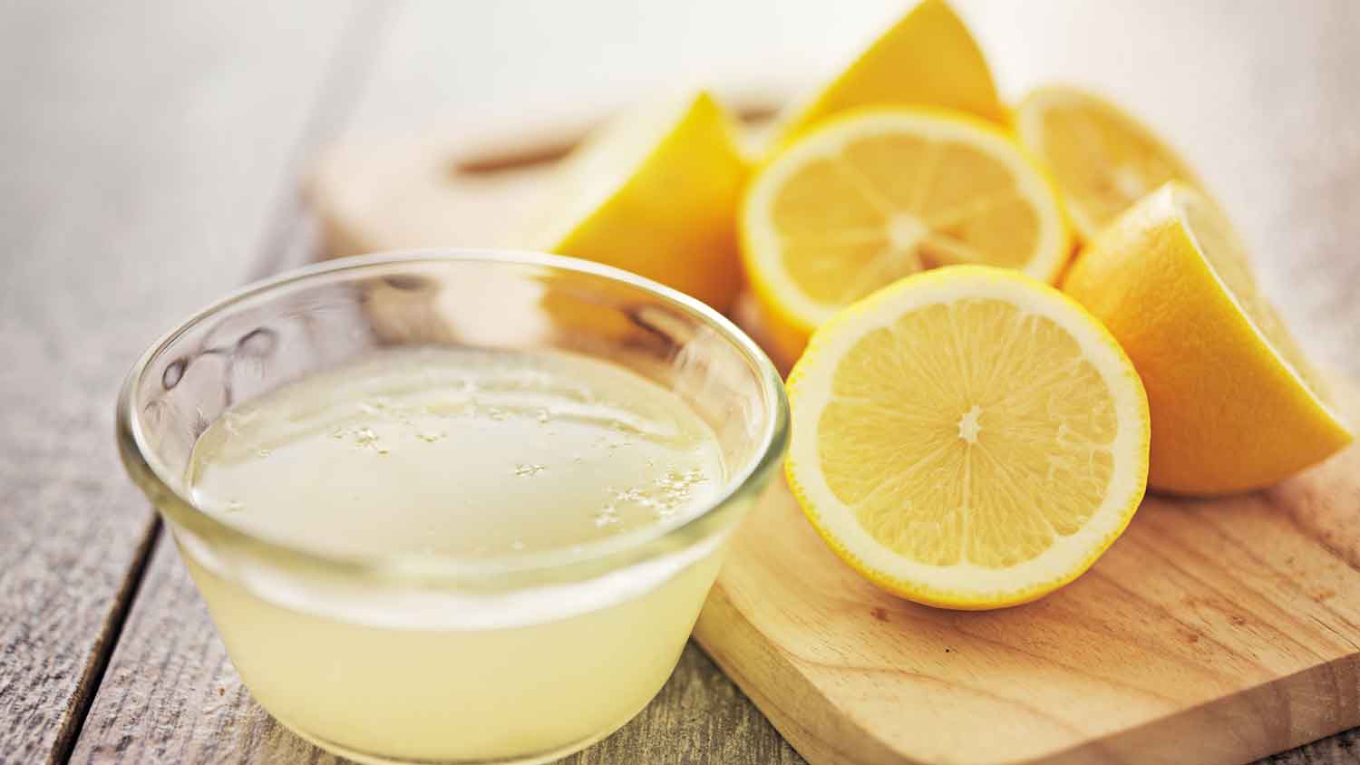 Bowl with natural lemon juice and lemons on a cutting board