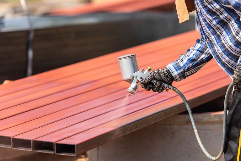 Worker spraying paint to steel pipe