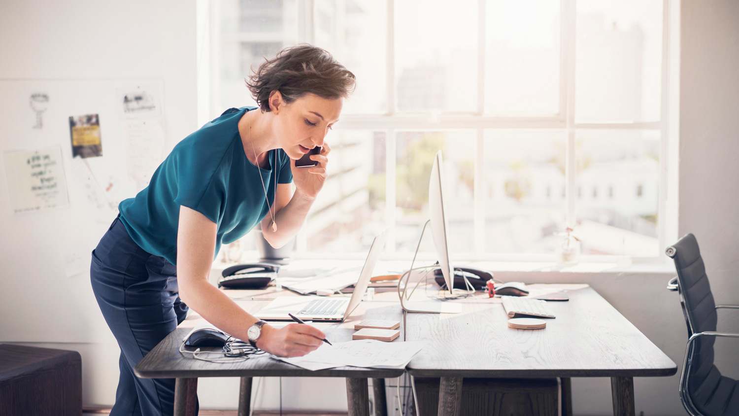 A woman taking notes while talking on the phone