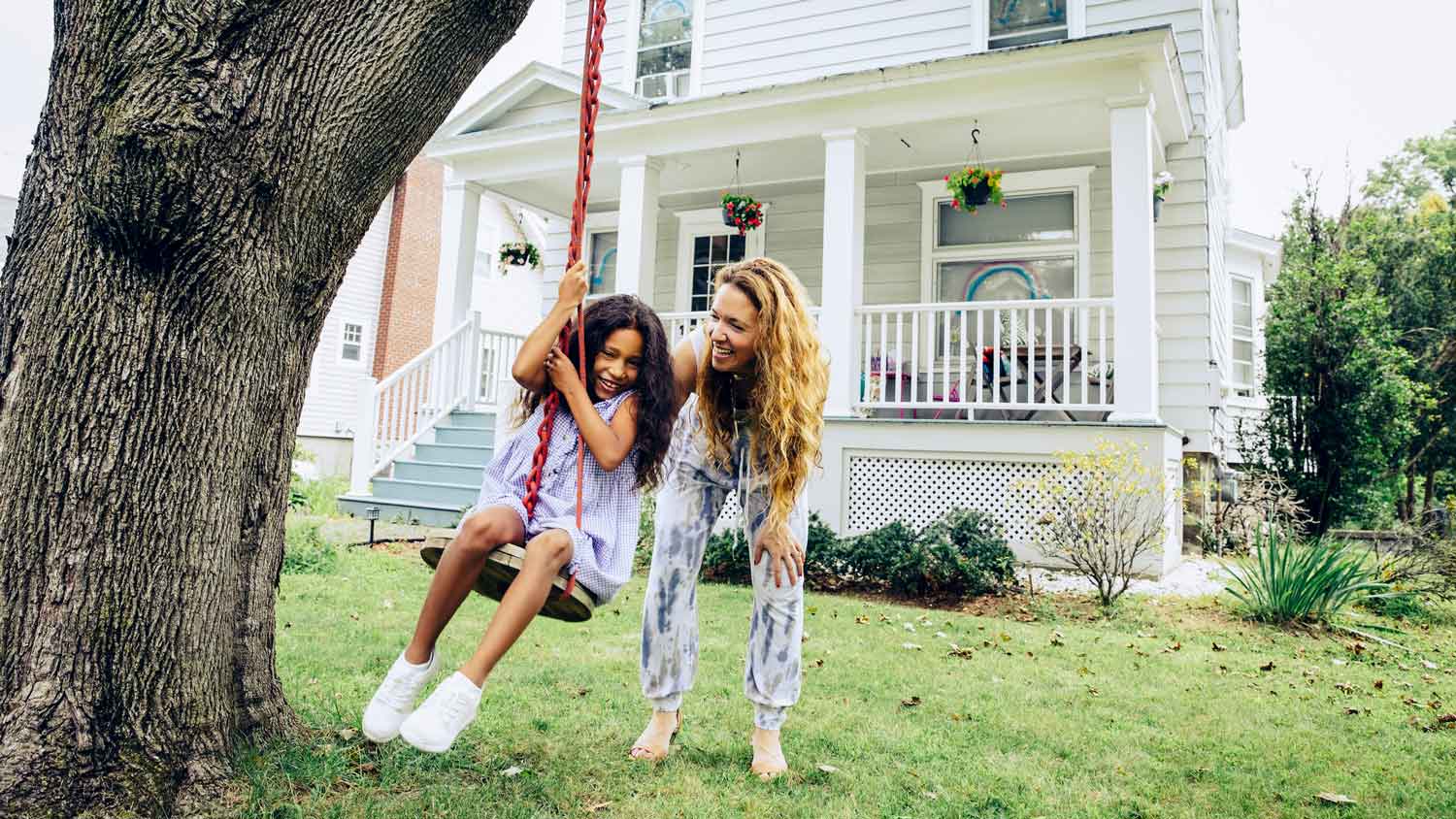 A mother pushing her daughter on a swing in their front yard