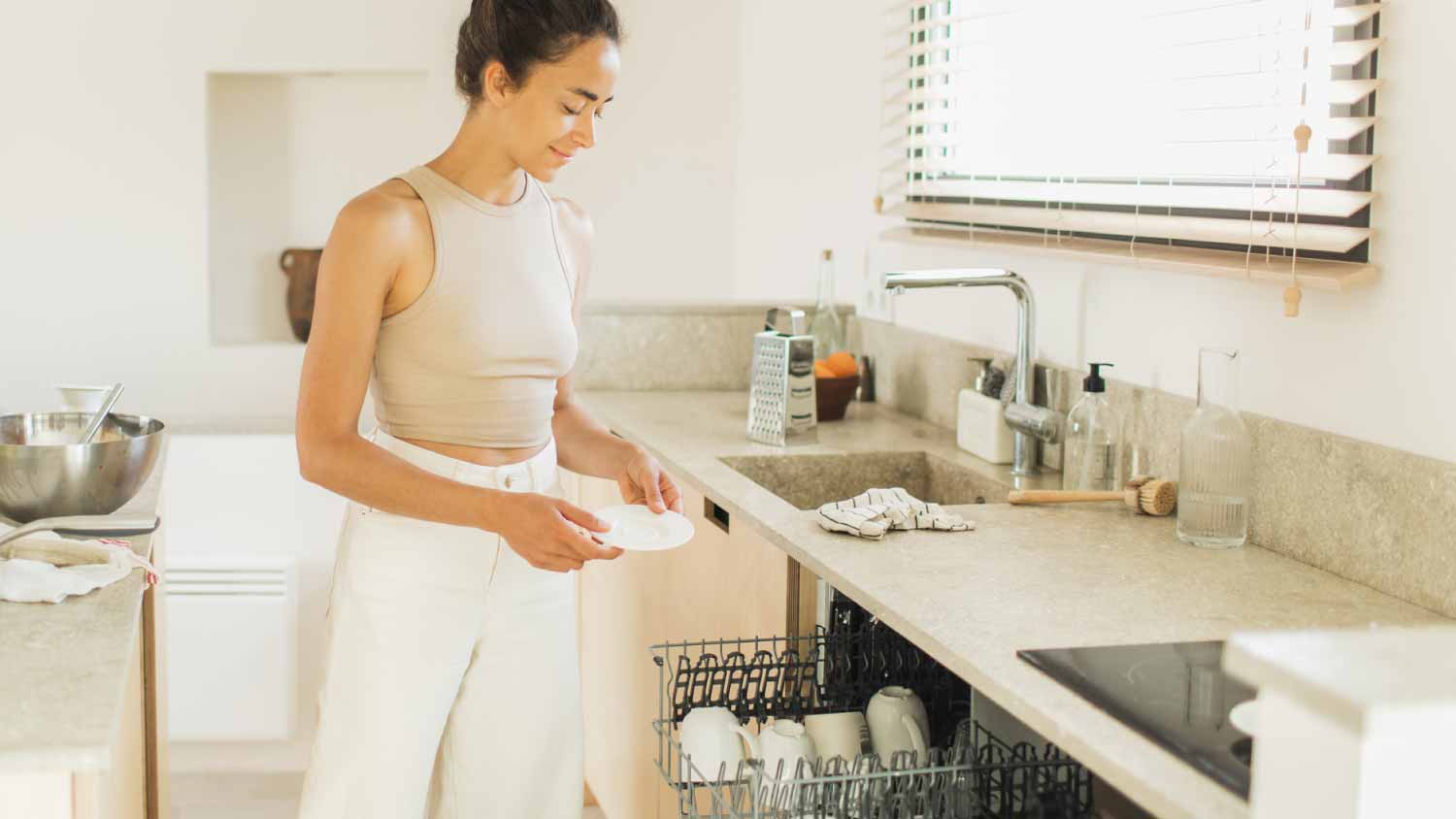 Woman loading plates and cups in the dishwasher