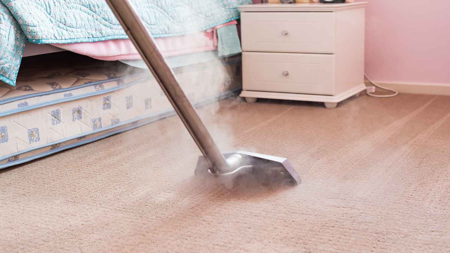 Worker steam cleaning carpet in a bedroom