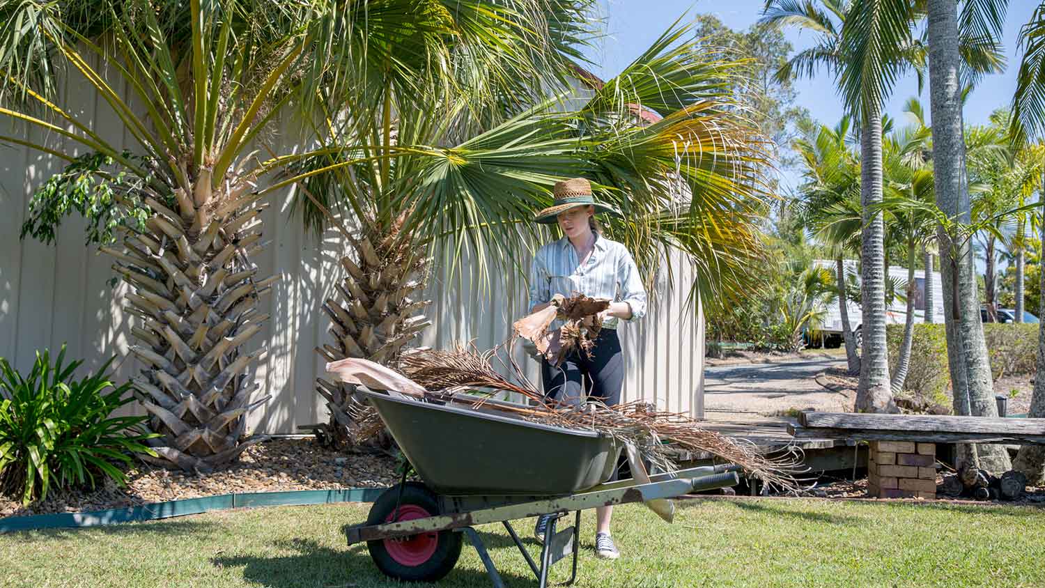 Woman placing palm fronds into a wheelbarrow
