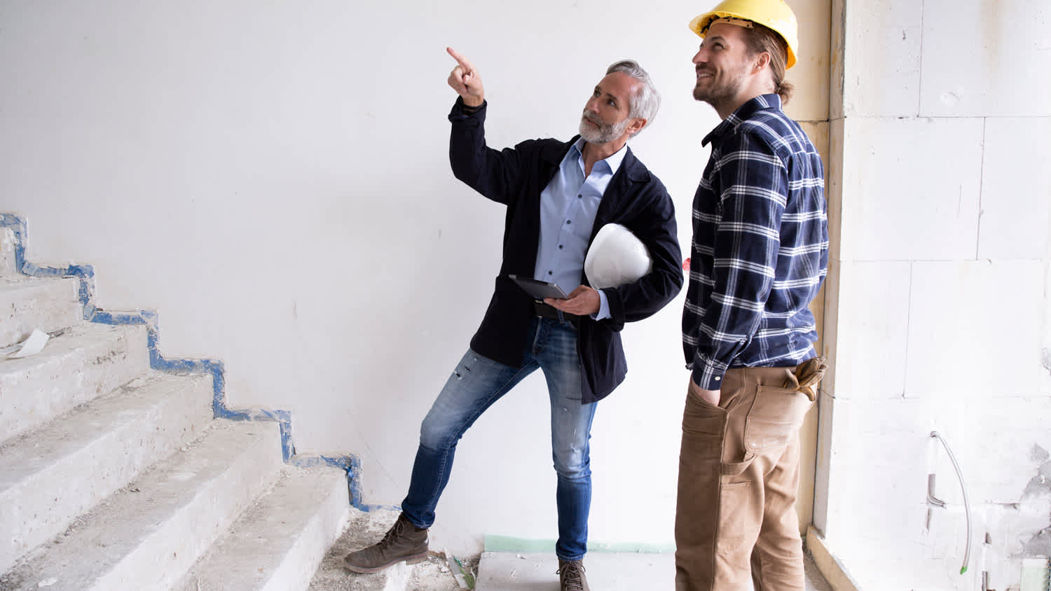 Male architect guiding construction worker while standing on steps in renovating house