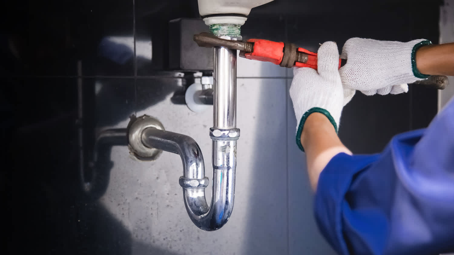 Close-up of a plumber’s hands in gloves fixing a sink pipe