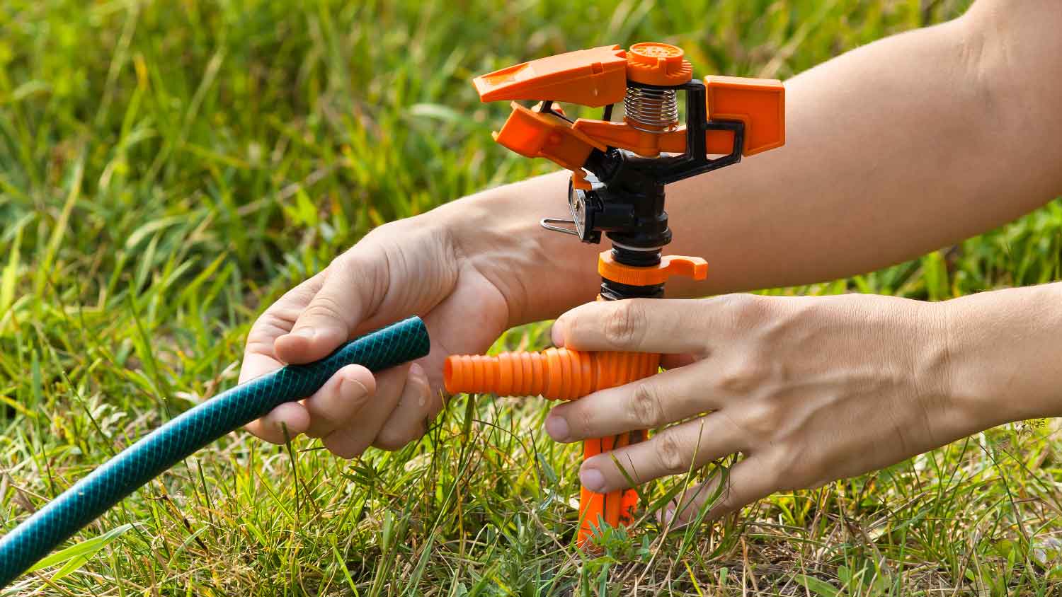 A person connecting a hose to a sprinkler head