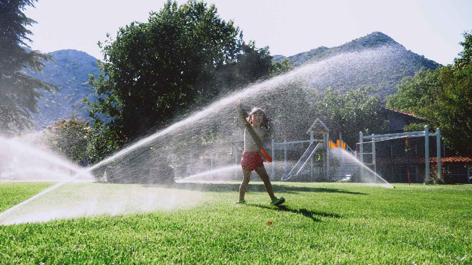 A kid playing while sprinklers are watering the lawn