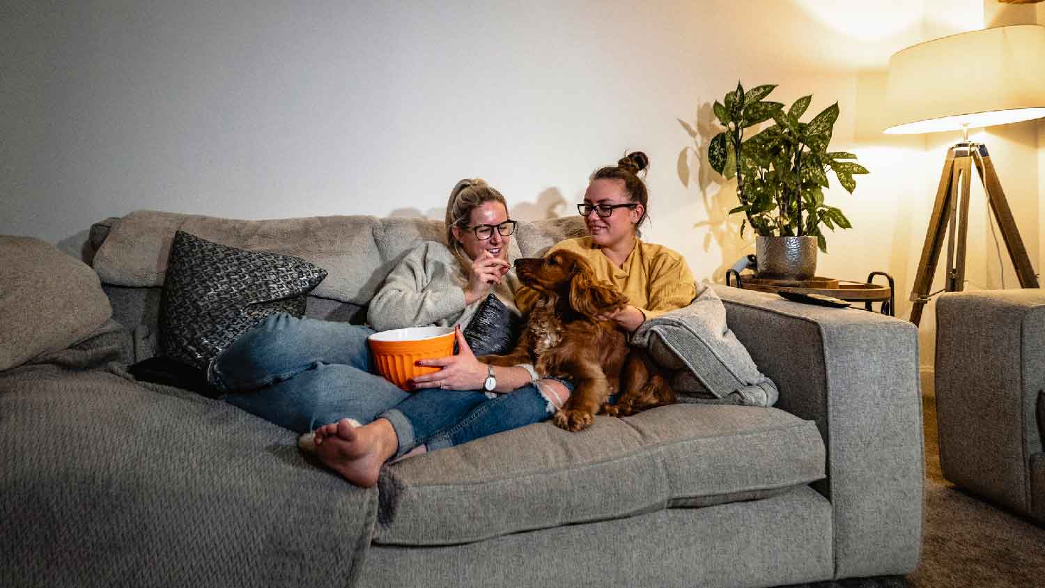 A couple with their dog on the sofa next to a floor lamp