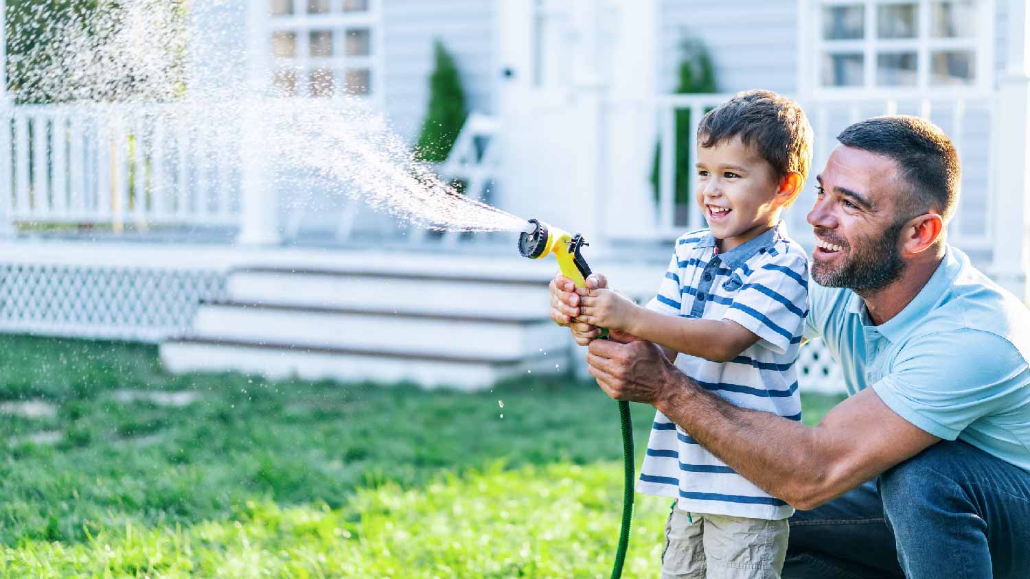 A father with his son splashing water with a hose