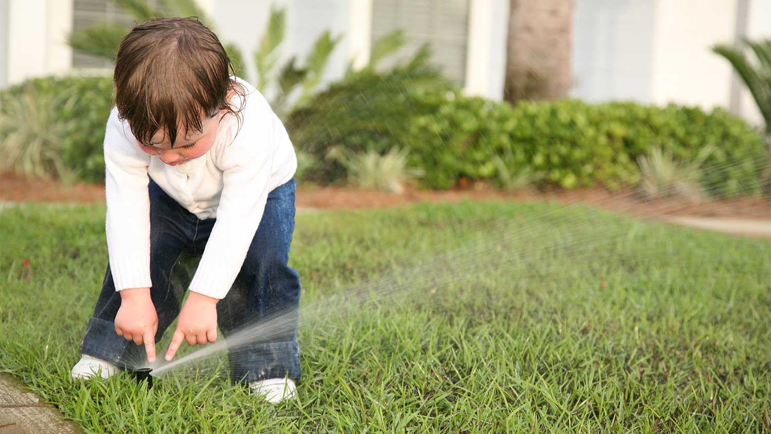 A toddler playing with sprinklers on a lawn