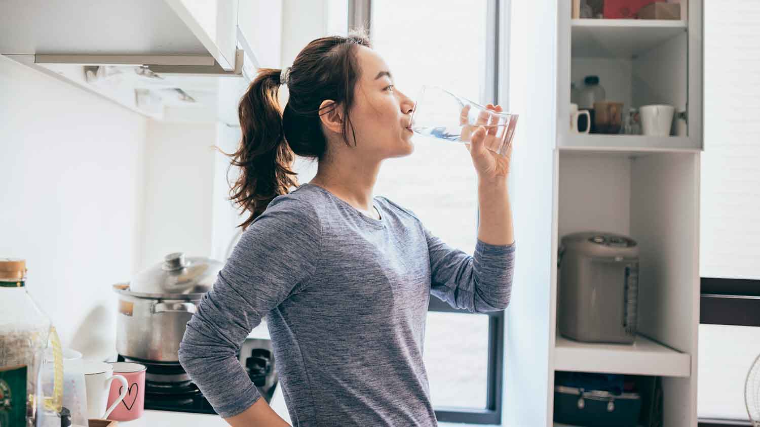 Young woman in the kitchen drinking water
