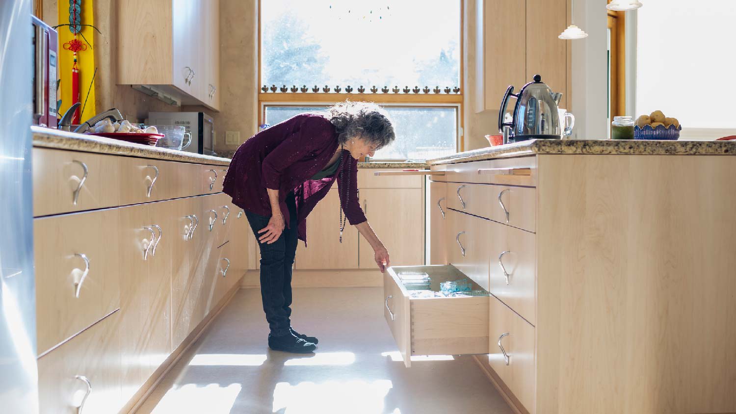 A woman opening a bottom drawer in her sunny kitchen