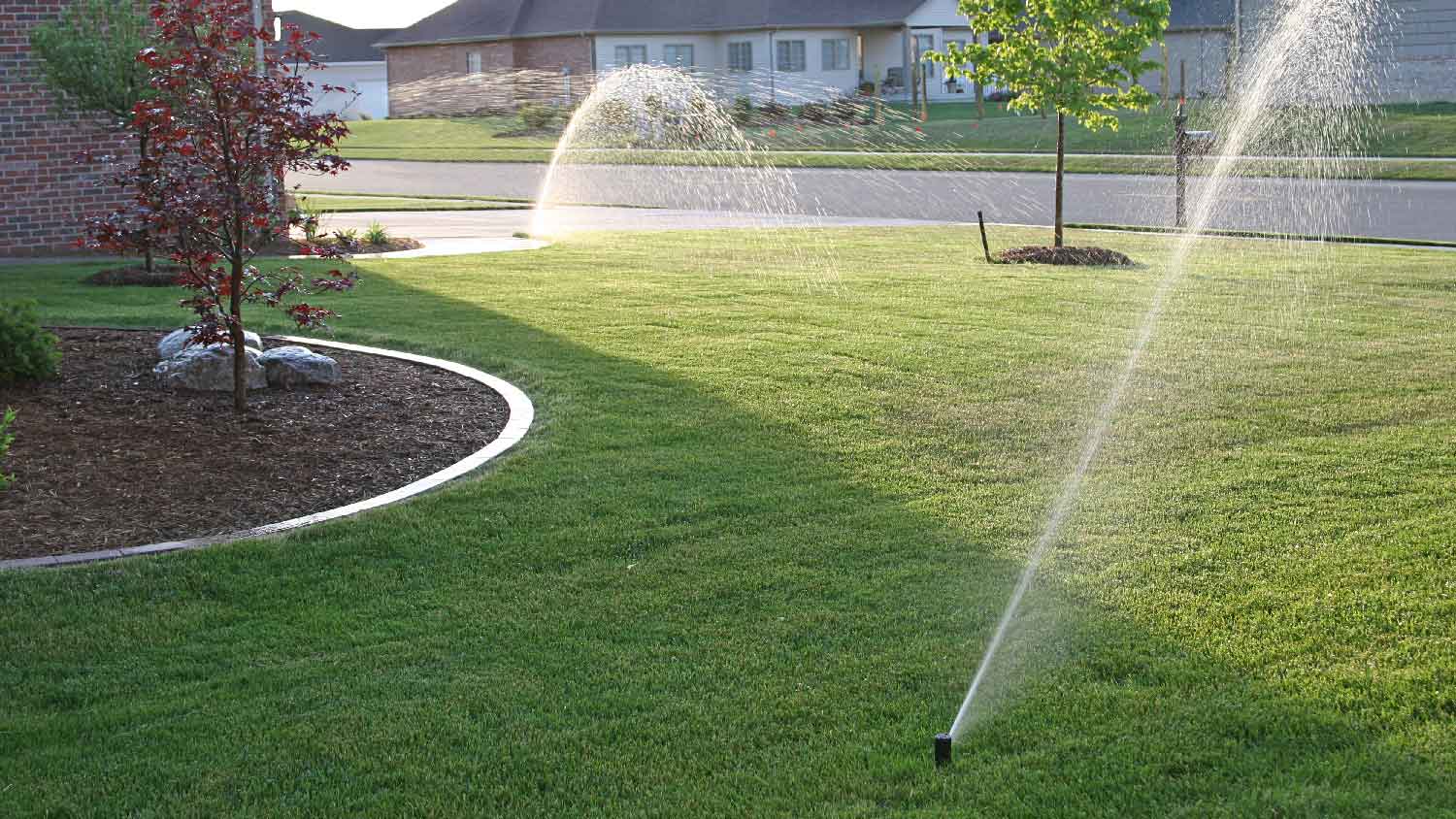 A sprinkler system watering the lawn on a house’s front yard