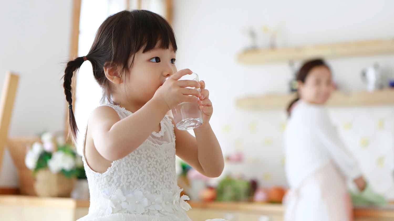 Little girl in the kitchen drinking water from a glass