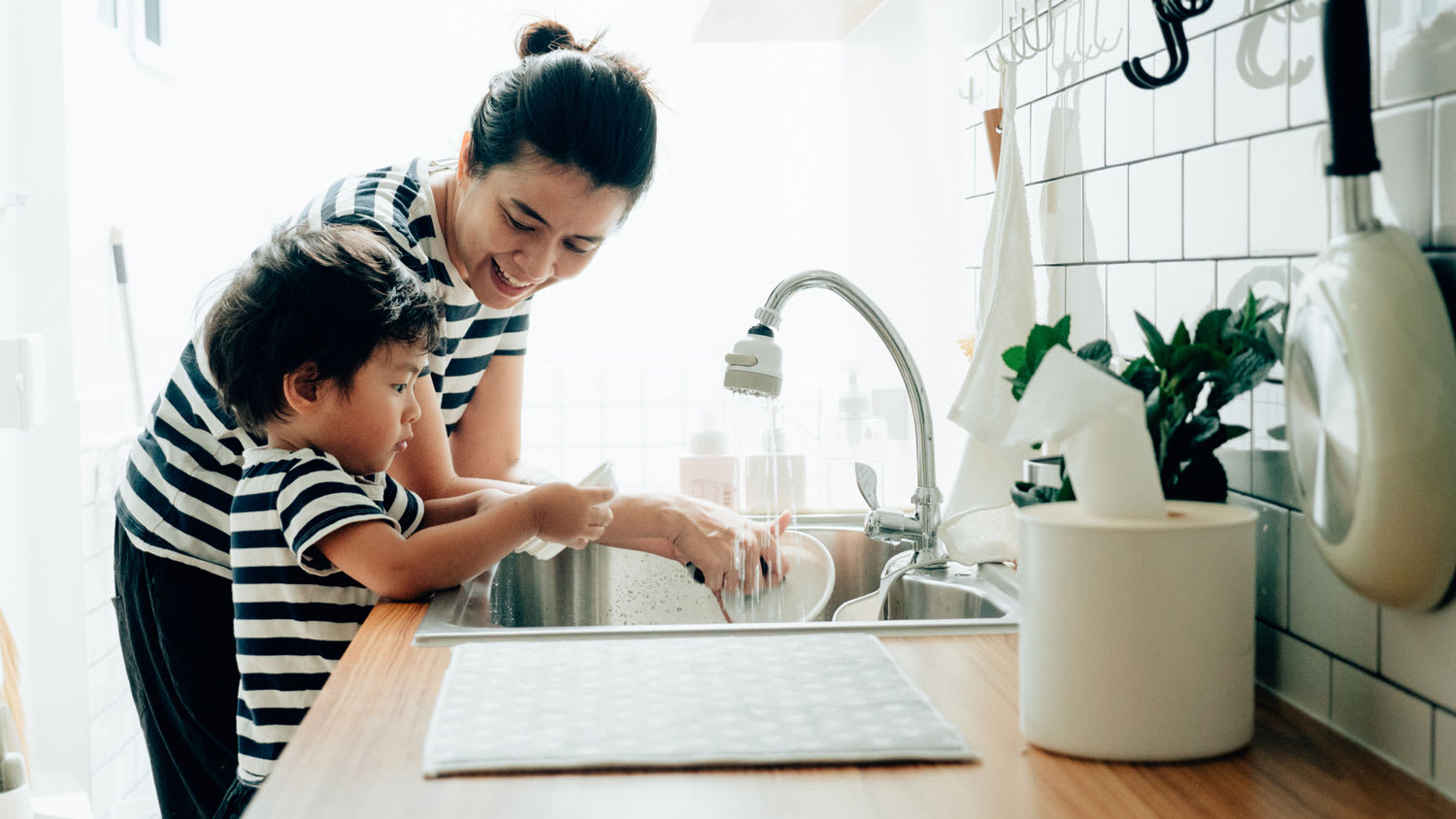 A mother and her son doing the dishes in the kitchen sink