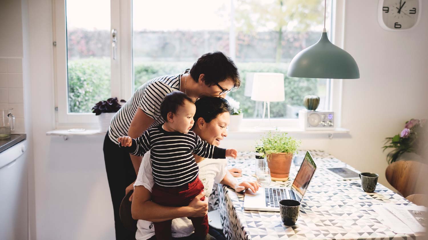 A family of three looking at laptop in the kitchen with a pendant light above