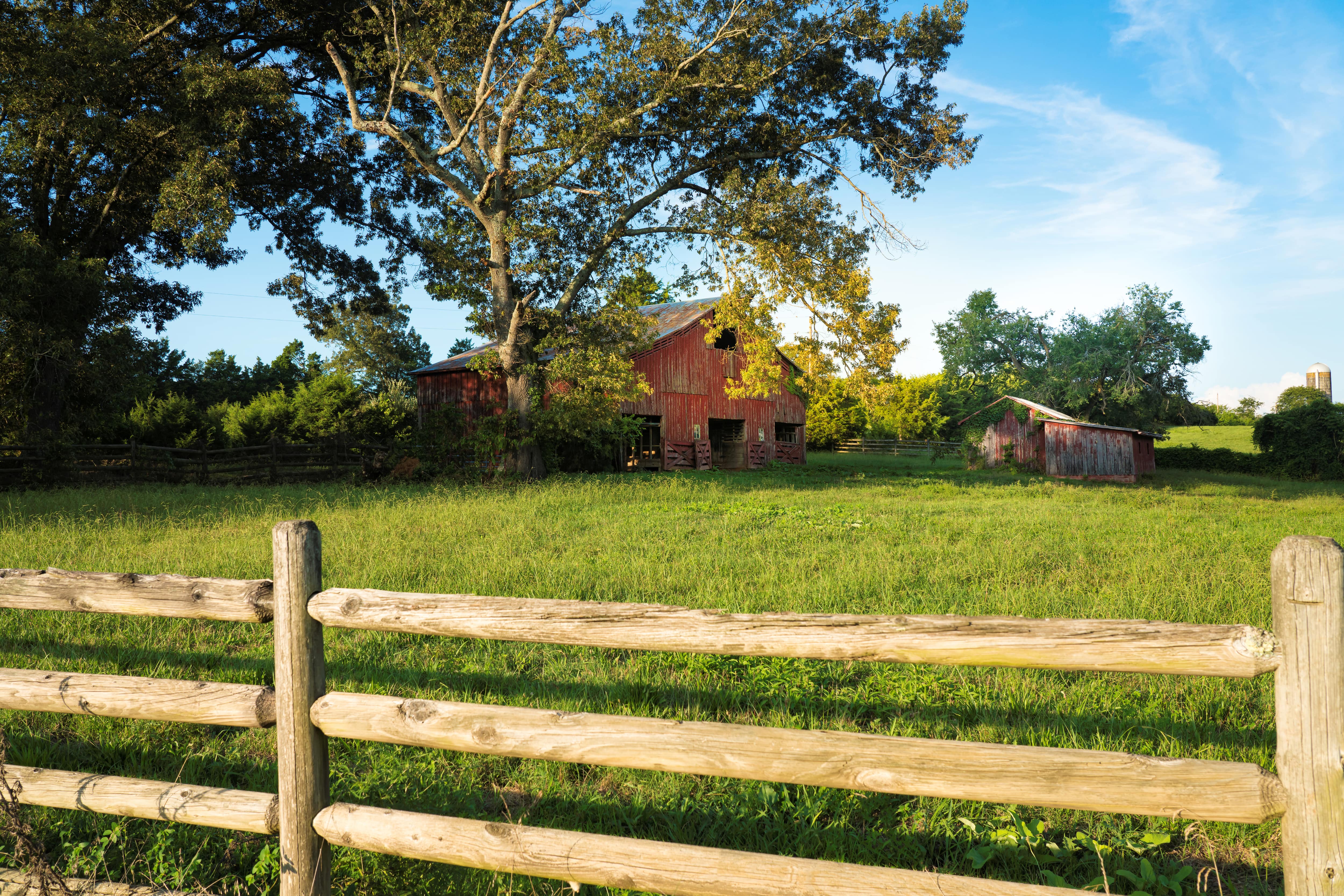 Closeup image of a front yard split-rail fence with a barn in the background