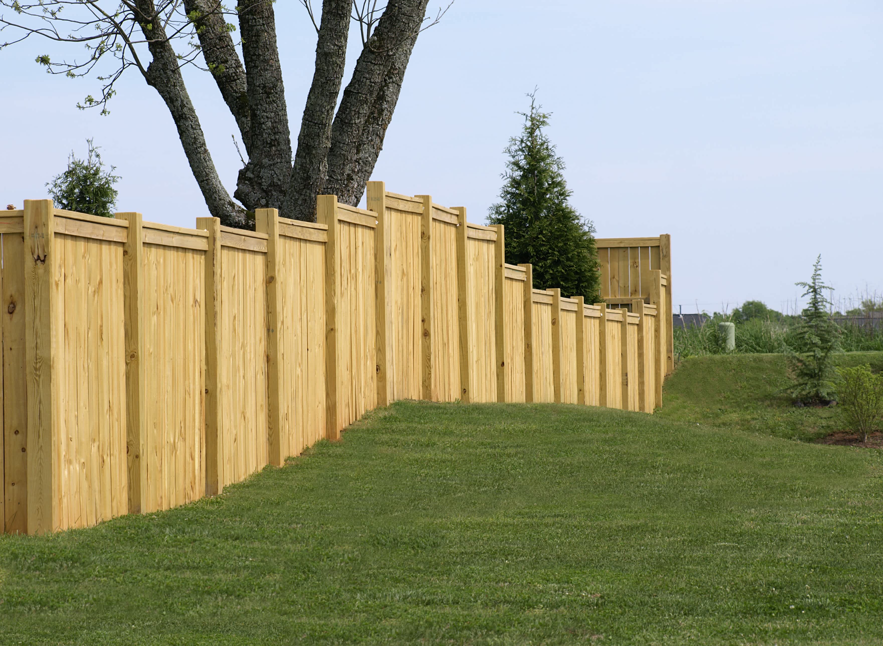 A tall natural wood fence with varying heights enclosing a yard