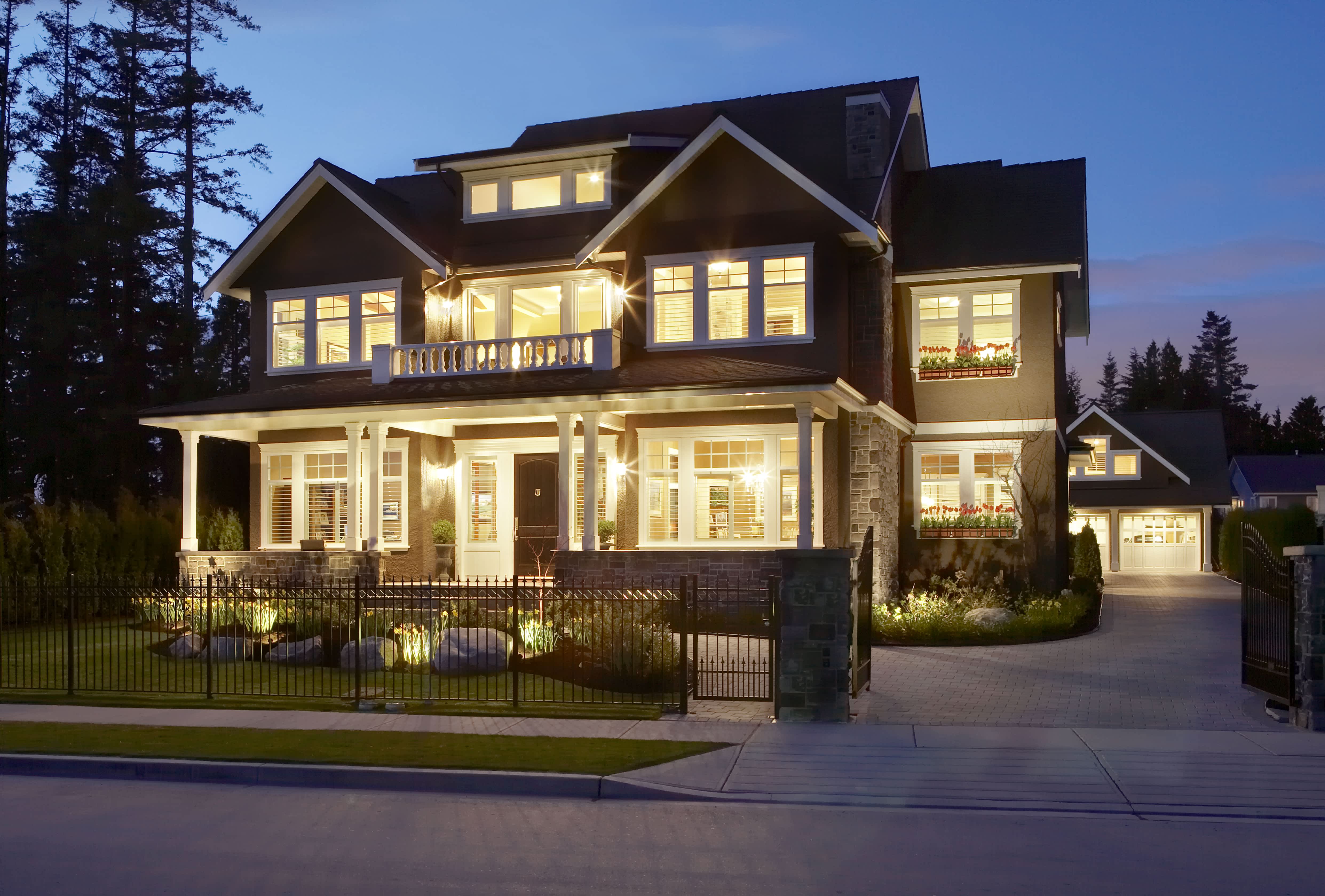 A house brightly lit at dusk with a wrought iron fence out front