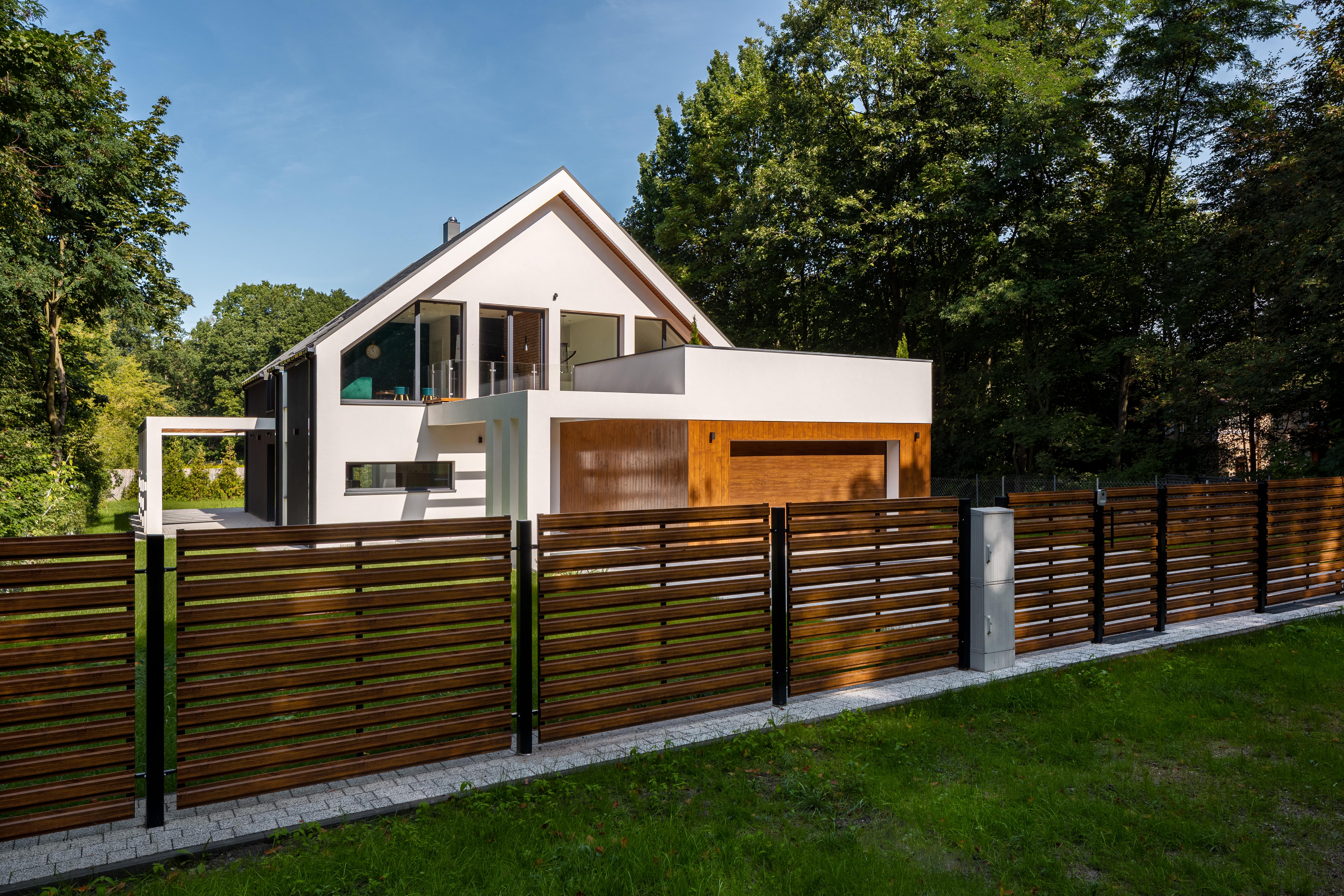 A modern fence made of wooden slats and iron bars in front of a modern home