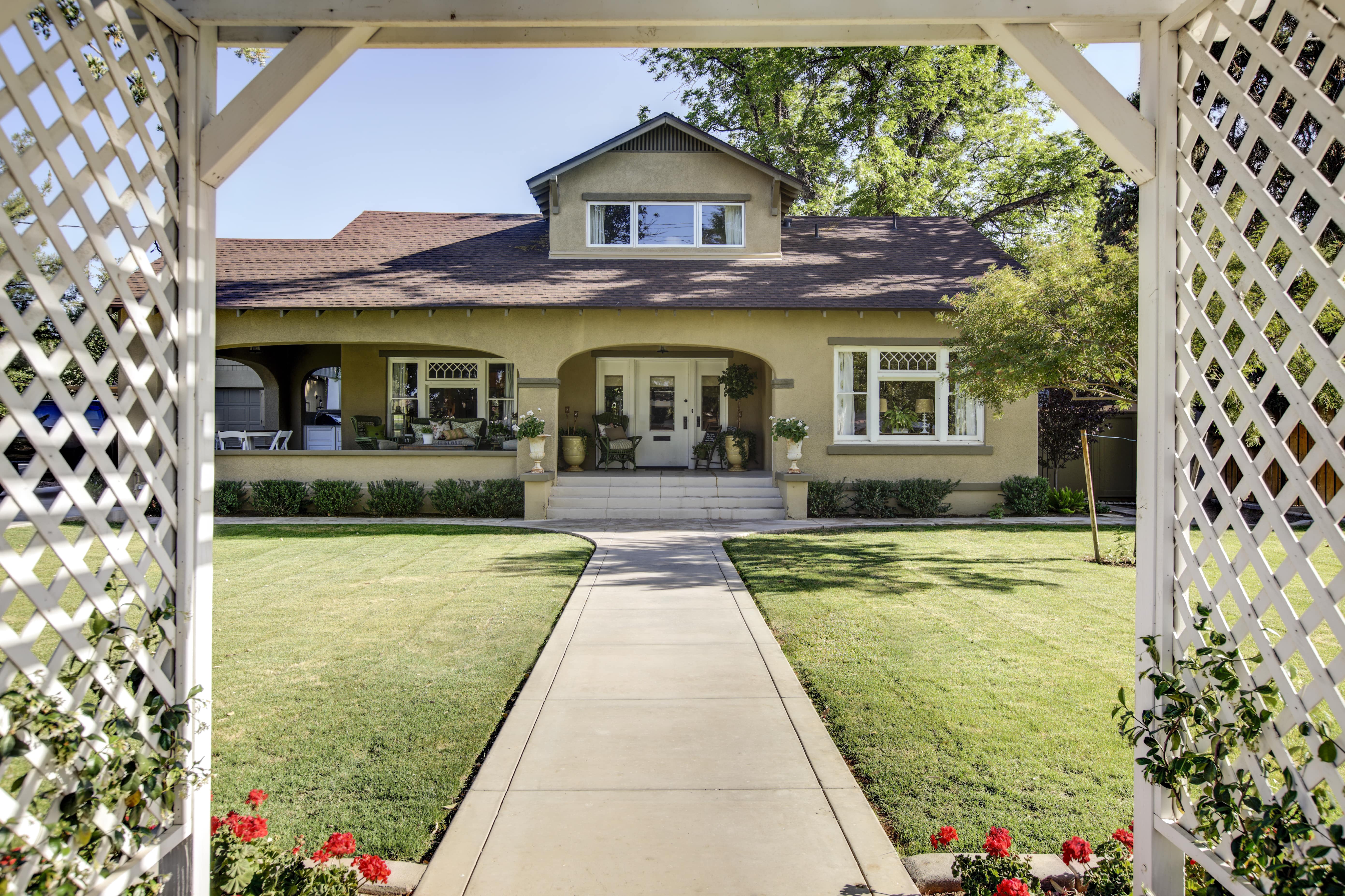 Photo peering through a front yard trellis fence and archway to the front of a house
