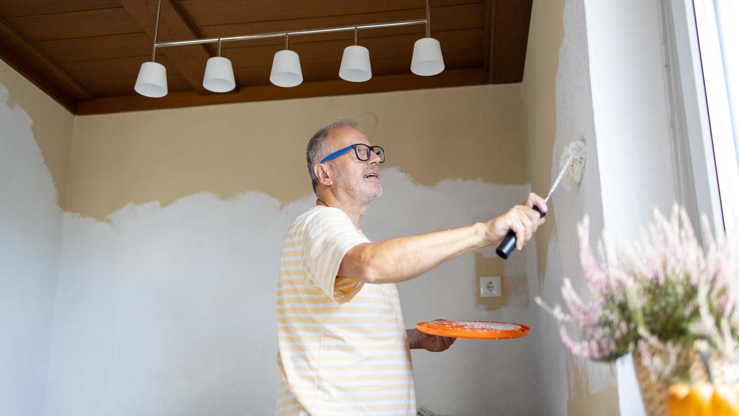 Mature man doing renovation at home while painting the wall with paint roller