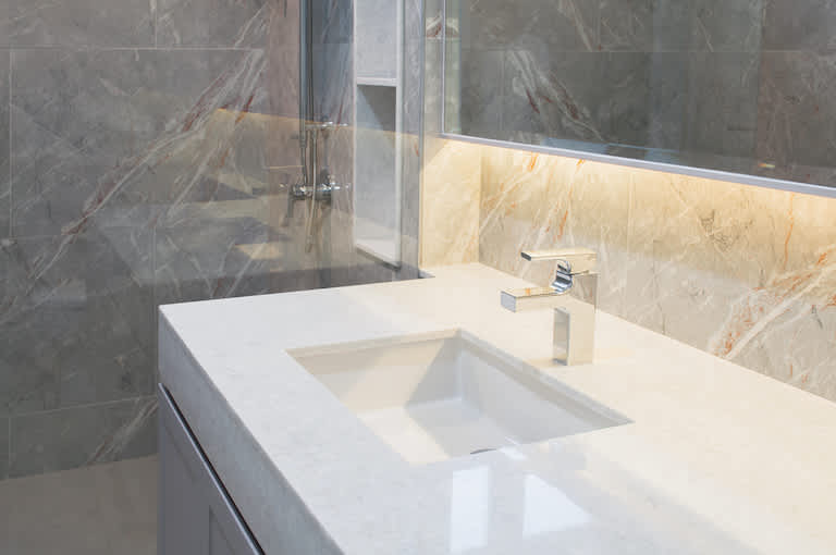 a white quartz bathroom countertop with rectangular shapes, silver fixtures, and tan and gray marbled walls