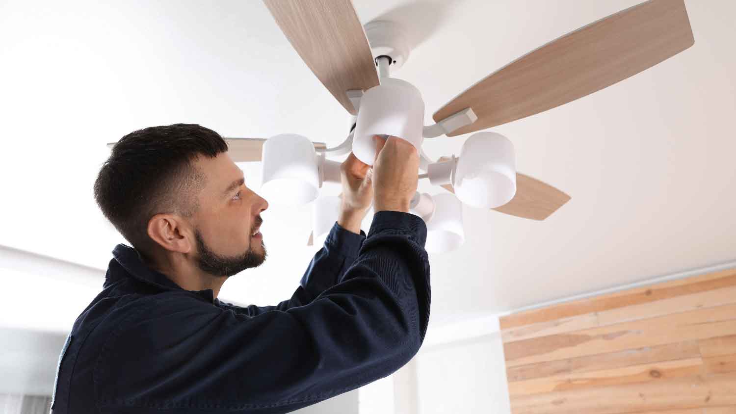 A person changing one of the light bulbs in the ceiling fan